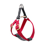 A red and black dog harness with beige plastic buckles and a silver metal D-ring at the top, shown against a plain white background.
